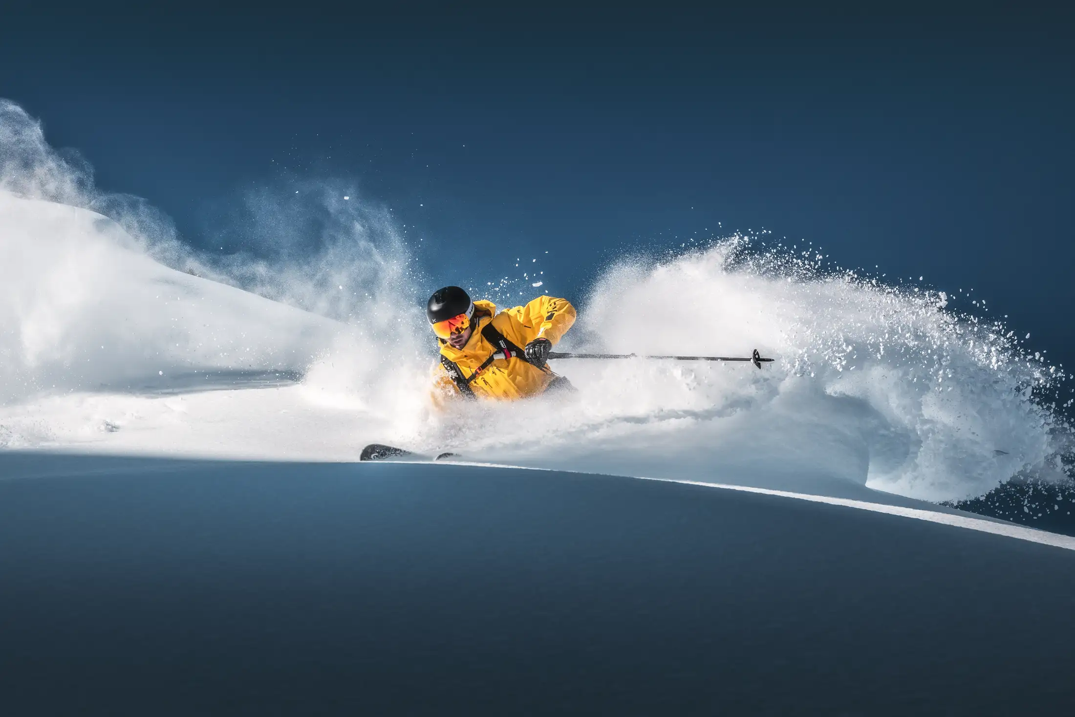 A skier cutting a line through deep fresh powder on a mountain slope